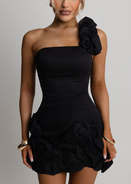 Women's black mini dress with one shoulder ruffle sleeve and ruffle detail on lower half of dress. Bodycon fit and structured fabric. Model is 5ft6' and wears a size XS.