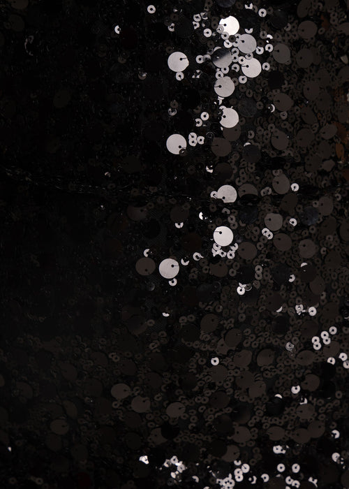 Close up fabric swatch of dress showing different sized black sequins and the shine on the sequins. 