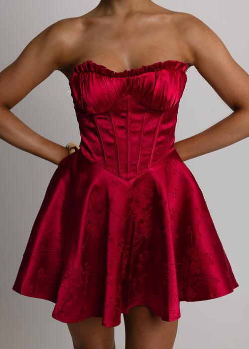 Women's red satin strapless mini dress with corset style bodice and floaty fit. Model is 5ft2' and wears a size XS.