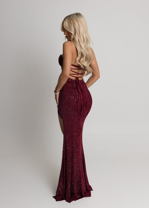 Women's burgundy maxi dress crafted with sparkle mesh fabric, thigh high slit and adjustable straps. Figure hugging fit and halter neckline.