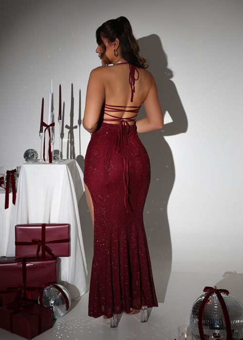 Women's burgundy maxi dress crafted with sparkle mesh fabric, thigh high slit and adjustable straps. Figure hugging fit and halter neckline.