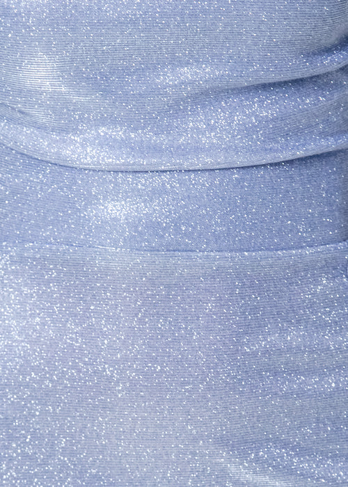 Woman standing against white backdrop in studio wearing a baby blue glittery gown with thigh high split,  spaghetti straps and figure hugging fit. 