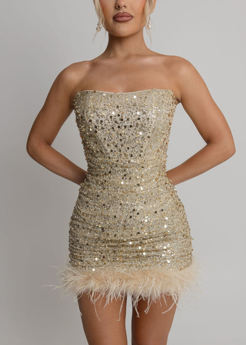 Women's gold sequin and feather mini dress with strapless design and feather trim hemline. Bodycon fit and lace up back. Model is 5ft2' and wears a size XS 6.
