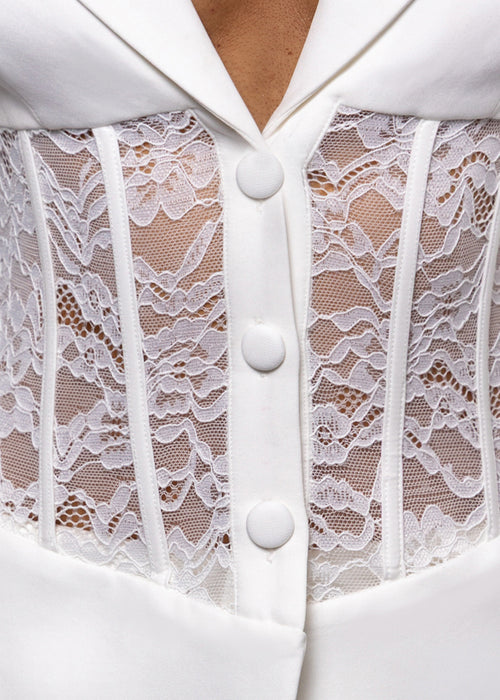 Close up detail of white lace fabric and white button fastening om blazer set. 